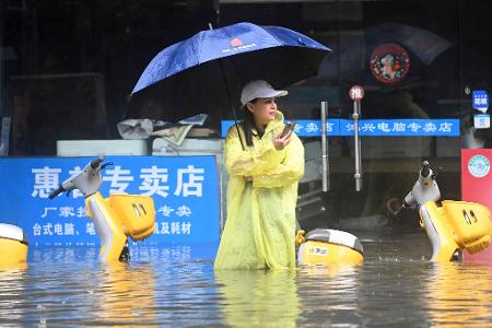 Eine Frau steht in Qinzhou auf einer mit Wasser vollgelaufenen Straße.
