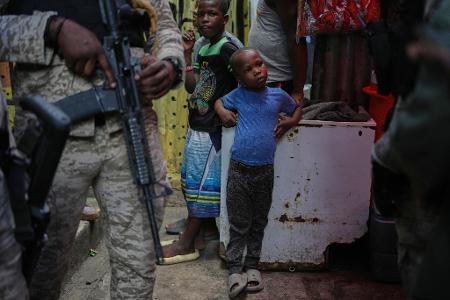 Kind neben bewaffnetem Polizisten in Unterkunft für Vertriebene in Port-au-Prince