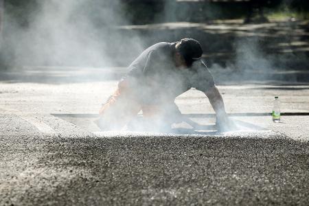 Ein Bauarbeiter repariert eine Straße in Berlin mit Bitumen, einem Bindemittel für Asphalt. (Symbolbild)
