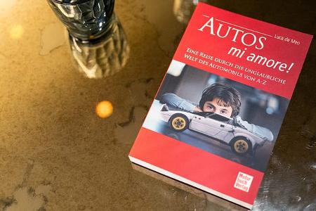Buchcover 'Autos mi amore!' von Luca de Meo auf einem Glastisch mit Wasserglas und Karaffe, fotografiert im Publicis Drugstore in Paris im Juli 2025.