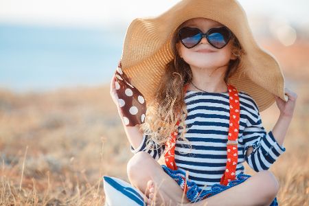 Kleines Mädchen posiert mit Sonnenhut und Sonnenbrille