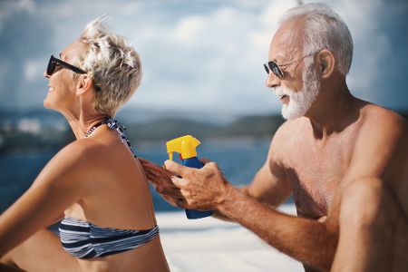 Altes Ehepaar cremt sich am Strand mit Sonnencreme ein