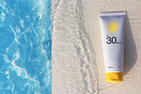 Sonnencreme mit LSF 30 liegt auf Sand neben Pool