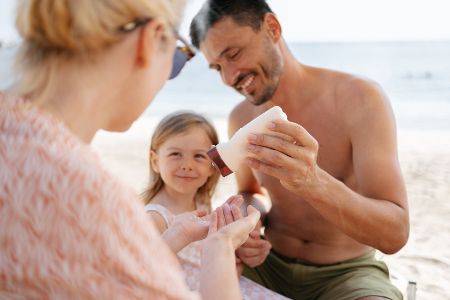 Familie mit Kind cremt sich mit Sonnencreme ein