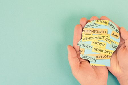 Zwei Hände halten ein Gehirn, in dem neurodivergente Begriffe stehen