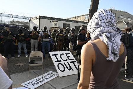Vor Bundesbeamten der Einwanderungsbehörde ICE haben Demonstrierende ein großes Schild mit der Aufschrift 