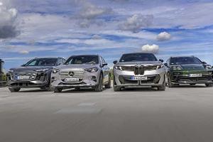 Vier Elektro-SUVs – Audi Q6 SUV e-tron quattro, BMW iX3 50 xDrive, Mercedes GLC 400 4matic EQ und Porsche Macan 4S – nebeneinander auf einer offenen Fläche, fotografiert aus niedriger Perspektive, mit Himmel und Wolken im Hintergrund.