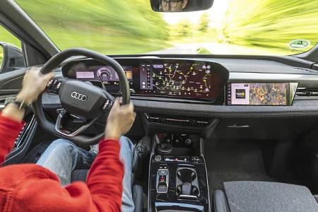 Innenraum und Cockpit des Audi Q6 SUV e-tron quattro während der Fahrt, Fokus auf digitales Armaturenbrett und Fahrer.