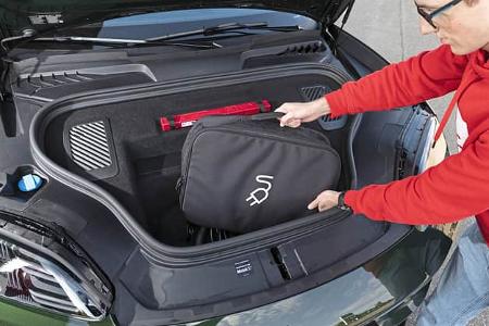 Ein Mann legt eine Tasche mit Ladesymbol in den vorderen Kofferraum eines Porsche Macan 4S.