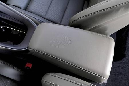 Detailaufnahme der Mittelarmlehne und Vordersitze eines Porsche Macan 4S. Das Porsche-Wappen ist auf der Lederarmlehne eingeprägt.