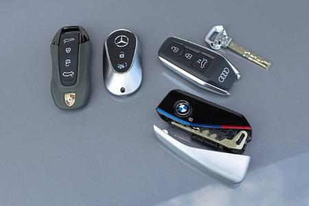 Vier Autoschlüssel von BMW, Mercedes-Benz, Audi und Porsche liegen nebeneinander auf einer glatten Oberfläche.