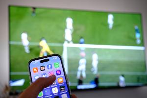 Nebenbei mal daddeln: Während das Fußballspiel läuft, schauen viele Zuschauer nebenbei aufs Handy. (Symbolbild)