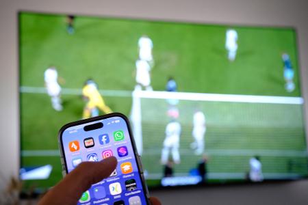 Nebenbei mal daddeln: Während das Fußballspiel läuft, schauen viele Zuschauer nebenbei aufs Handy. (Symbolbild)