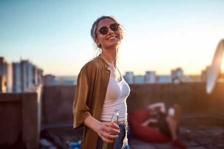Frau mit Sonnenbrille und Flasche in der Hand auf einem Hausdach in der Stadt