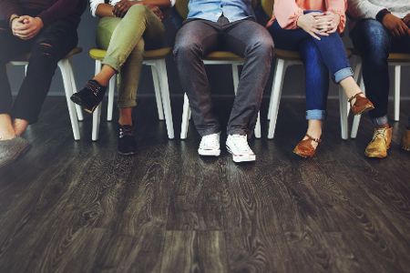 Füße von verschiedenen Personen nebeneinander auf einer Stuhlreihe