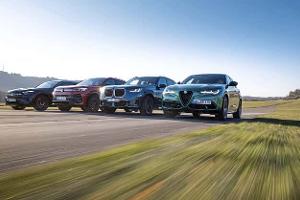 Vier Mittelklasse-SUVs – Mercedes GLC 220d 4Matic, BMW X3 xDrive 20d, Alfa Romeo Stelvio 2.0 Diesel und VW Tiguan 2.0 TDI – fahren nebeneinander auf einer Landstraße.