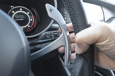 Detailaufnahme des Schaltwippen-Bereichs am Lenkrad eines Alfa Stelvio 2.0 Diesel. Die rechte Hand bedient die Schaltwippe, im Hintergrund sind das Kombiinstrument und Bedienelemente sichtbar.