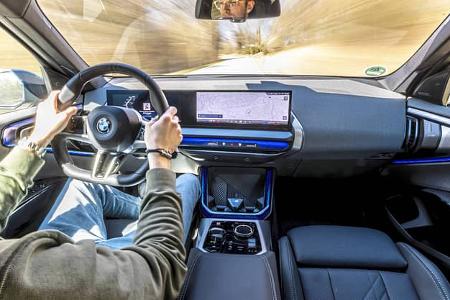 Innenraum des BMW X3 xDrive 20d während der Fahrt, Blick über die Schulter des Fahrers auf das Cockpit und das zentrale Infotainmentsystem.