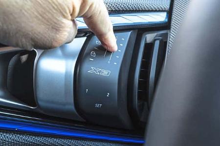 Detailaufnahme des Innenraums eines BMW X3 xDrive 20d, Fokus auf Bedienelement mit X3-Logo und Finger, der eine Einstellung vornimmt.