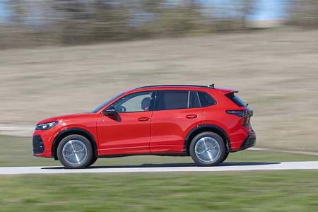 Seitenansicht eines roten VW Tiguan 2.0 TDI in Fahrt auf einer Landstraße, aufgenommen im Frühjahr 2024.