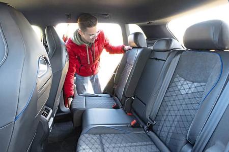 Innenraumaufnahme eines VW Tiguan 2.0 TDI, Fokus auf die Rücksitzbank. Eine Person im roten Anorak klappt die Rücksitzlehne um.