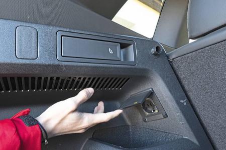 Detailaufnahme des Kofferraums eines VW Tiguan 2.0 TDI mit geöffneter 230V-Steckdose und Sitzentriegelung.