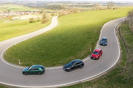 Vier Mittelklasse-SUVs (Mercedes GLC 220d 4Matic, BMW X3 xDrive 20d, Alfa Stelvio 2,0 Diesel, VW Tiguan 2.0 TDI) fahren in einer Kurve auf einer Landstraße durch hügelige Landschaft.