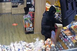 Der maskierte Täter bei der Tatausführung. In der rechten Hand hält er ein Messer.
