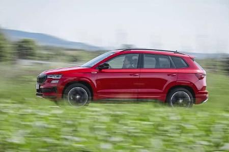 Rotes Skoda Karoq 4x4 SUV fährt seitlich durch grüne Landschaft, Bewegungsunschärfe im Hintergrund.