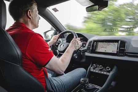 Innenaufnahme eines fahrenden Skoda Karoq 4x4 mit Fahrer, Blick auf Cockpit, Lenkrad und Infotainmentsystem.