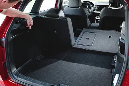 Der Kofferraum eines Skoda Karoq 4x4 mit umgeklappter Rückbank, ein Mann zeigt auf eine Funktion im Laderaum.