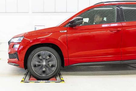 Rotes Skoda Karoq SUV, Seitenansicht, auf Rollenprüfstand in heller Werkstattumgebung, Fahrer am Steuer.