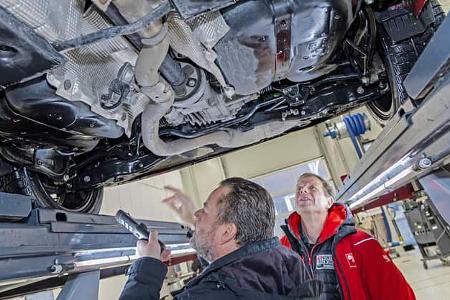 Zwei Personen inspizieren den Unterboden eines Skoda Karoq auf einer Hebebühne in einer Werkstatt.