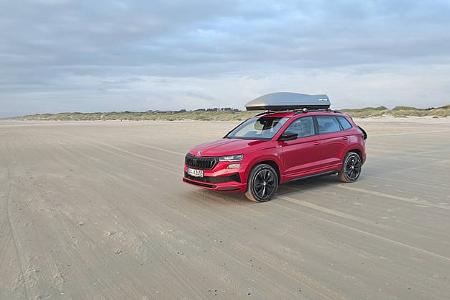 Skoda Karoq 2.0 TDI Sportline 4x4 (Modelljahr 2025) in Rot mit Dachbox auf Sandstrand, Aufnahme aus dem Dauertest.