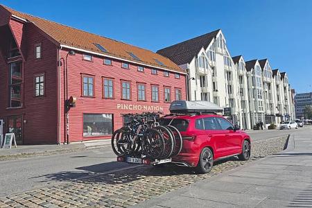 Skoda Karoq 2.0 TDI Sportline 4x4 (Modelljahr 2025) mit Fahrradträger und Dachbox vor städtischer Kulisse, aufgenommen im Rahmen eines Dauertests.