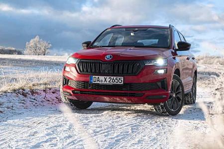 Roter Skoda Karoq 2.0 TDI 4x4 auf verschneiter Landstraße in winterlicher Landschaft, Frontalansicht.