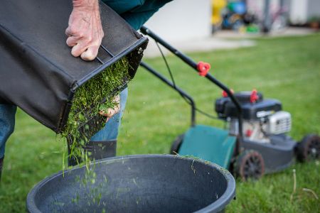 Mann schüttet nach dem Rasenmähen Grasschnitt in eine Tonne