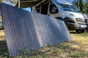 Tragbares Solarpanel auf dem Boden vor einem Campingbus im Wald.