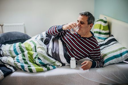 Älterer Mann liegt im Bett und nimmt Medikamente