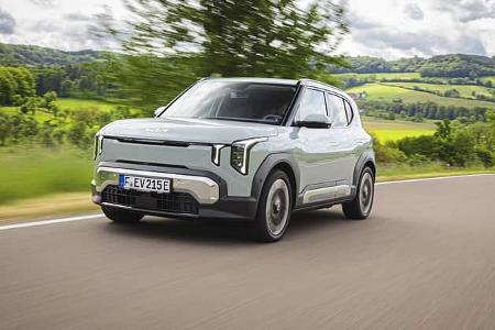 Kia EV2 auf Landstraße in Bewegung, ländliche Umgebung, modernes Elektroauto, Frontansicht.