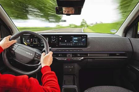Innenaufnahme eines fahrenden Kia EV2, Blick über die Schulter des Fahrers auf das Cockpit und die digitale Instrumententafel.