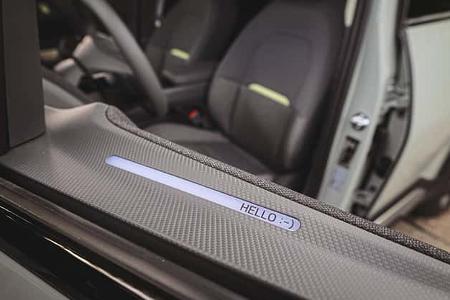 Detailaufnahme des Innenraums eines Kia EV2, Fokus auf Begrüßungs-Display am Seitenfenster mit 'HELLO :-)'-Anzeige.