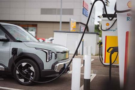 Kia EV2 RG26 beim Ladevorgang an einer Shell Recharge Ladestation auf einem Parkplatz, seitliche Frontansicht.