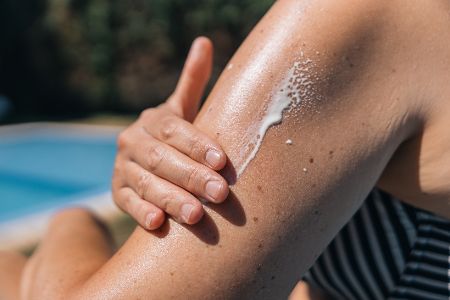 Frau cremt sich Oberarm mit Sonnencreme ein