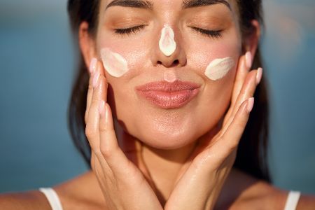 Frau cremt sich Gesicht mit Sonnencreme ein
