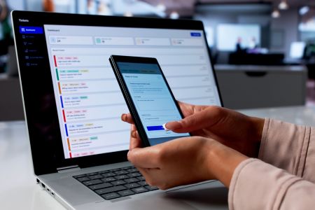 Mensch mit Handy in der Hand vor einem Computer