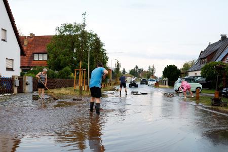 Anwohner versuchen nach einem schweren Gewitter in Erlangen die Wassermassen von der Straße zu schieben.