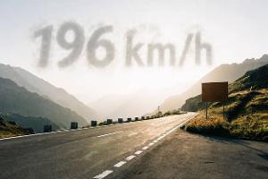 Der Sustenpass in der Schweiz im Sonnenuntergang, es spiegelt sich das Licht in der Straße auf dem kein Auto fährt, im Himmel darüber erscheint als Wolke "196 km/h"