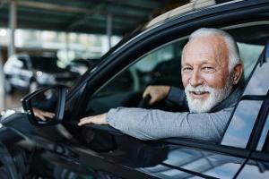 Ein älterer Mann mit weißem Bart am Steuer eines Pkw schaut lächelnd aus einem geöffneten Autofenster