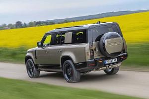 Land Rover Defender 130 D250 fährt auf einer Landstraße an einem blühenden Rapsfeld vorbei.